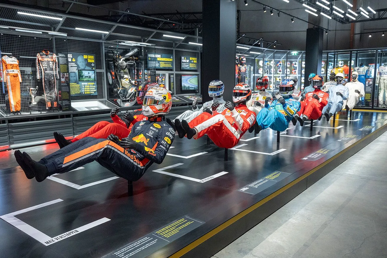 Driver figures in racing overalls posed in mid-air along an exhibition hall at F1 The Exhibition
