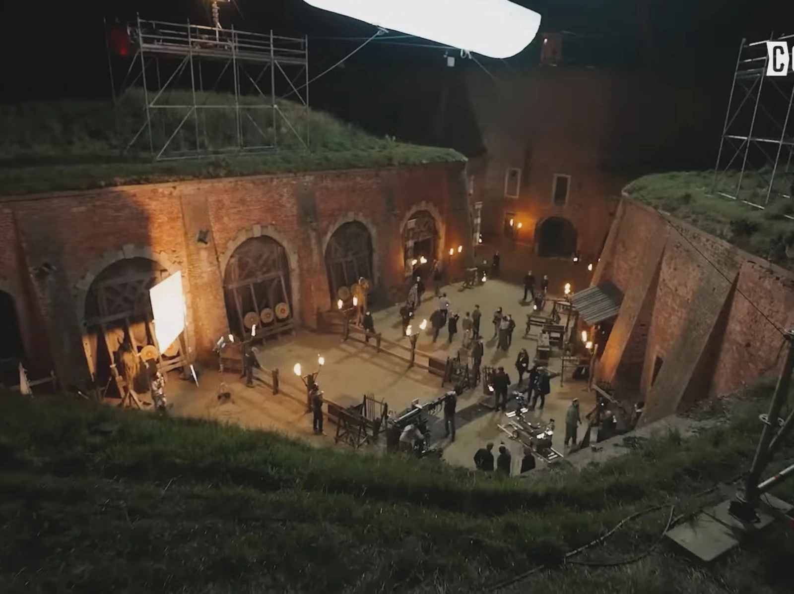 Film crew on a night set in a brick courtyard beneath a suspended soft light on The Wheel of Time